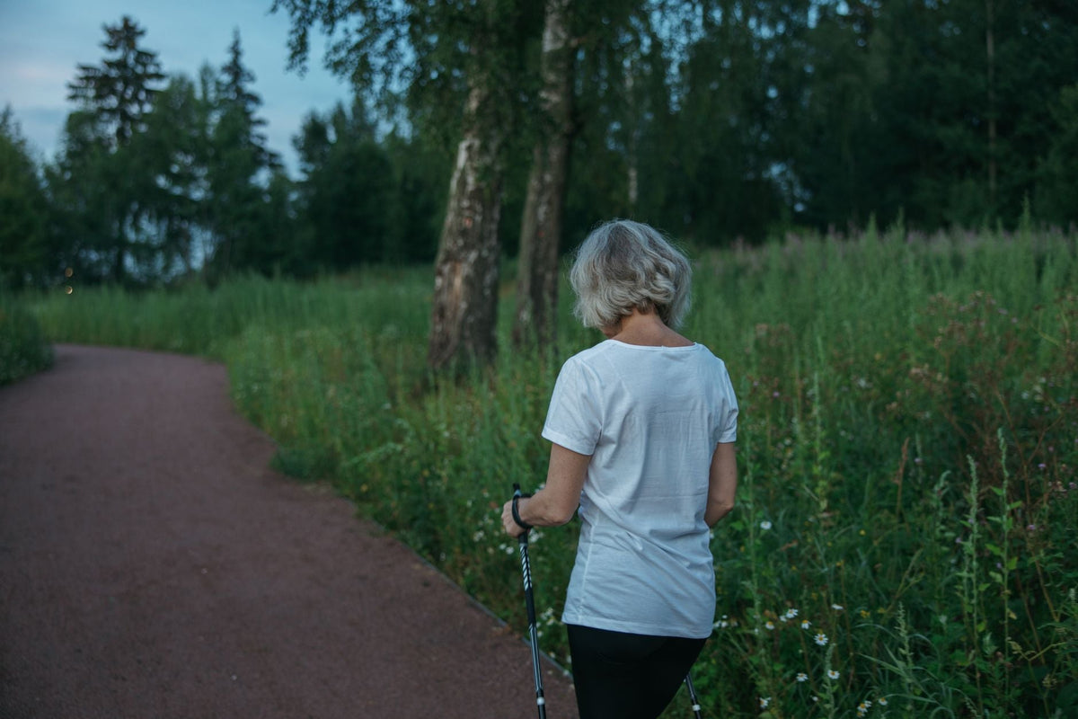 Frau von hinten geht auf einem Gartenweg zwischen grünen Pflanzen